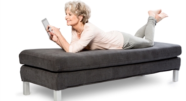 Lady is lying on couch, checking the webshop on her tablet. This image is used as keyvisual for the Homecare Benelux webshop.